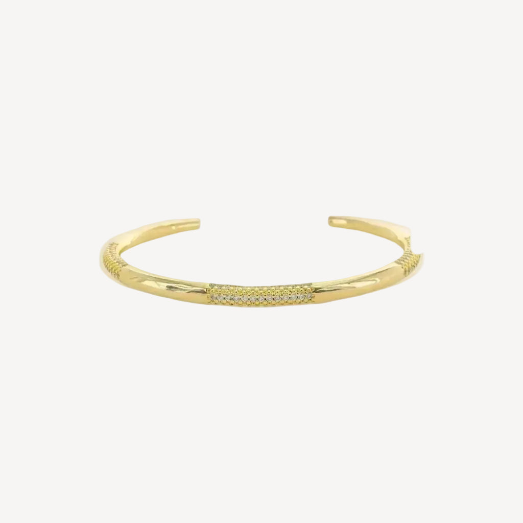 Gold cuff bracelet with small cubic zirconium stones on a white background
