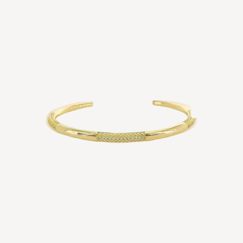 Gold cuff bracelet with small cubic zirconium stones on a white background