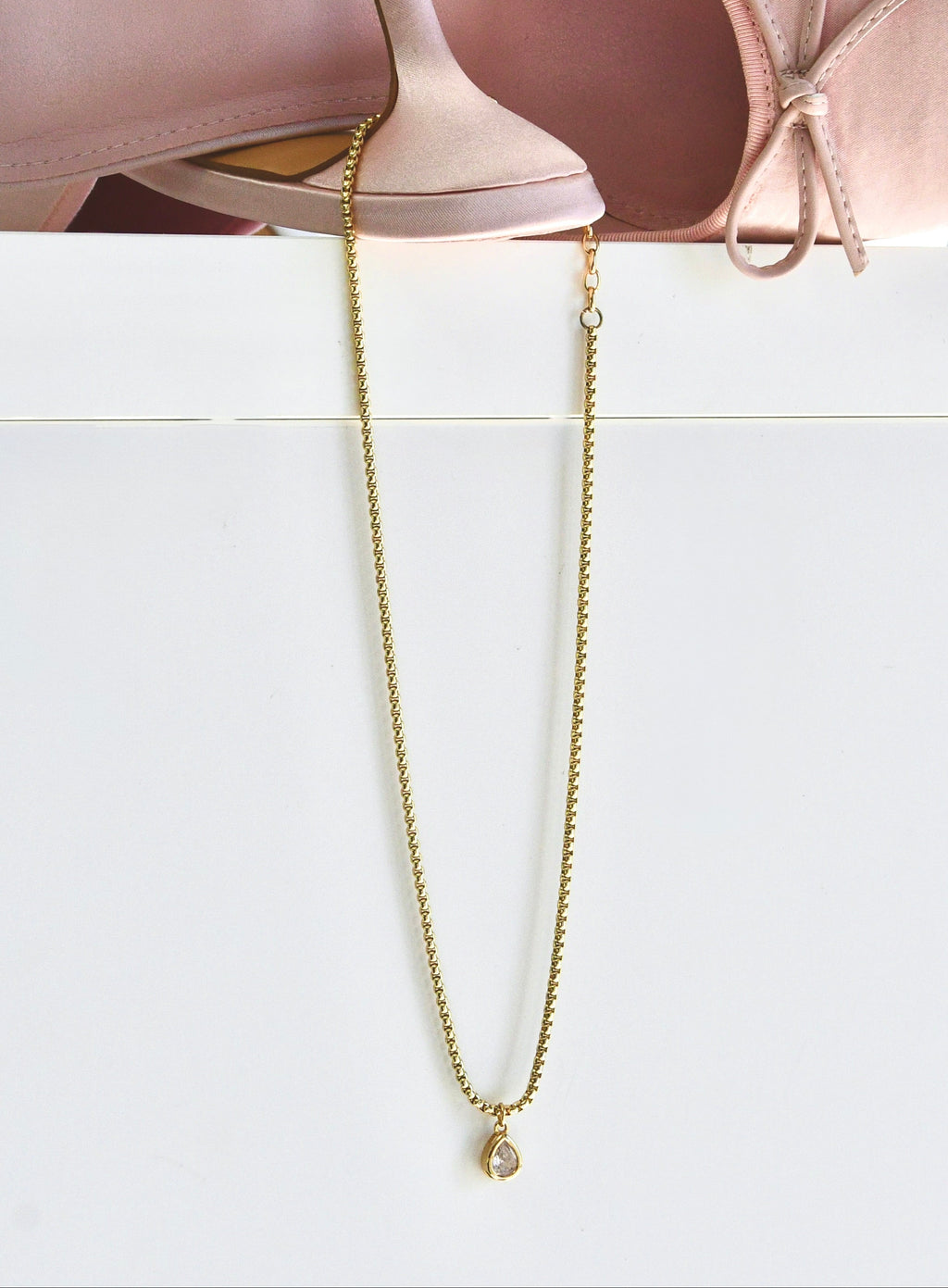 Gold chain necklace on a white surface with pink ballet shoes in the background
