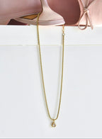 Gold chain necklace on a white surface with pink ballet shoes in the background