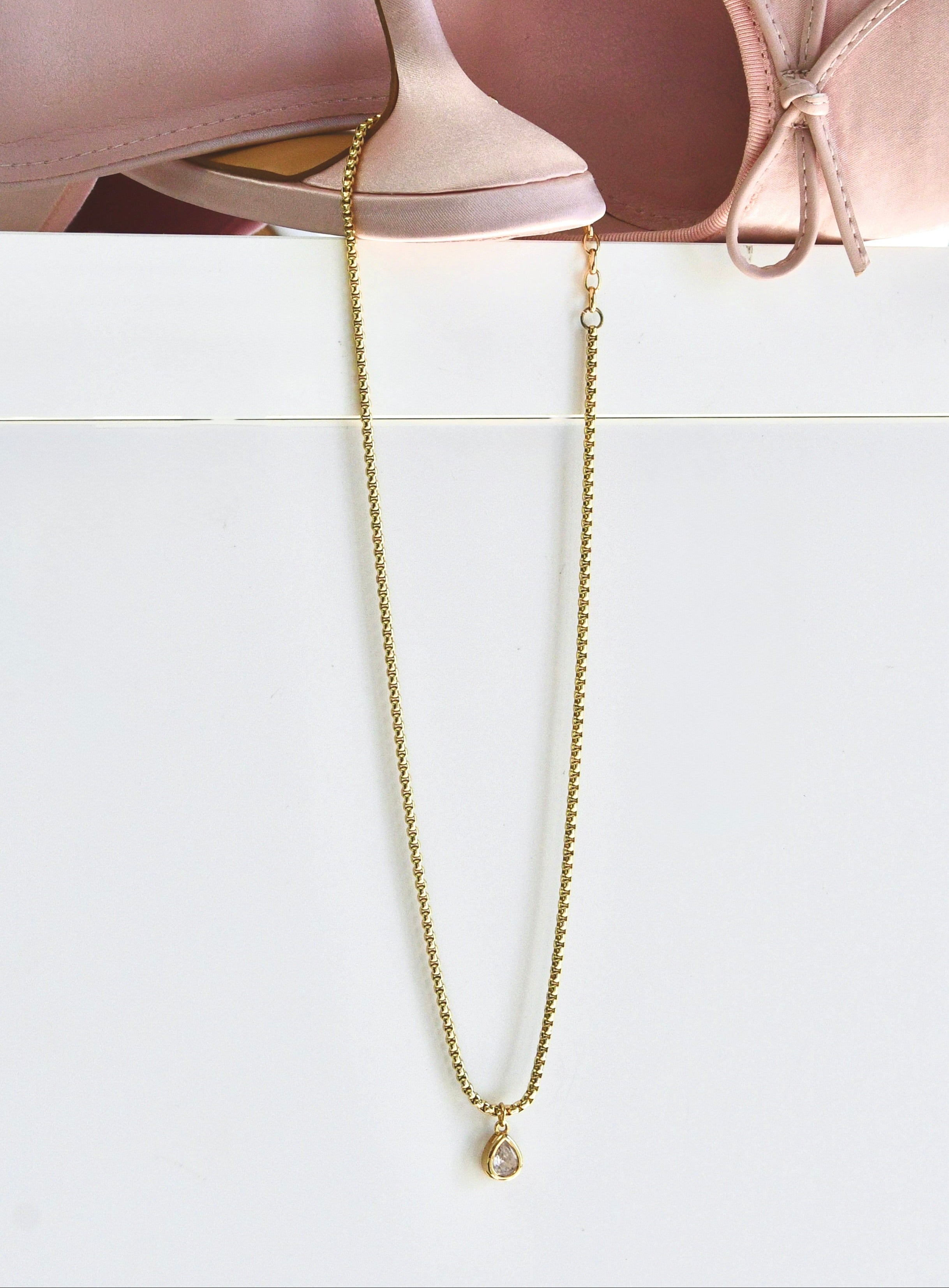 Gold chain necklace on a white surface with pink ballet shoes in the background