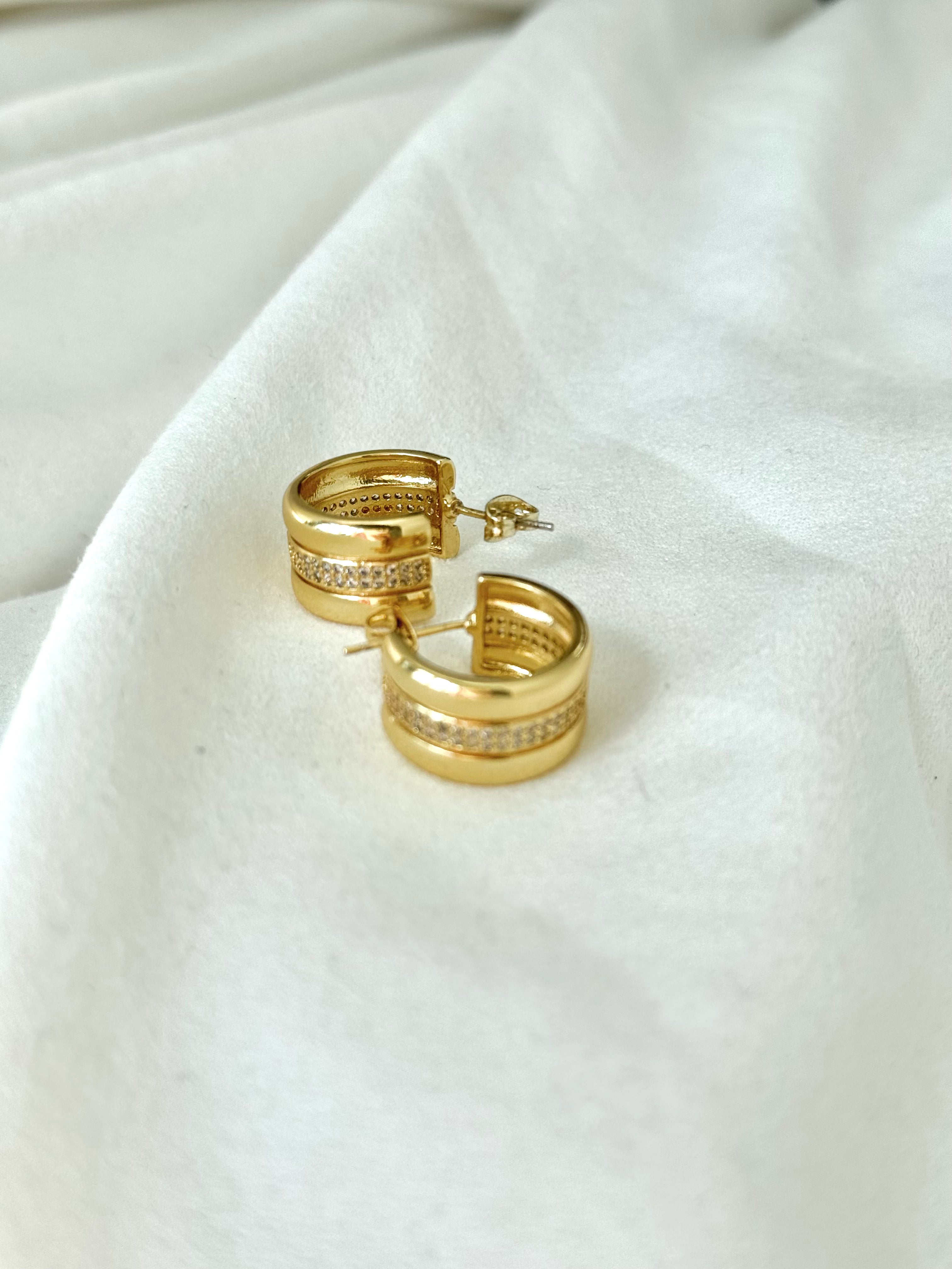 Gold hoop earrings with embedded stones on a white fabric background